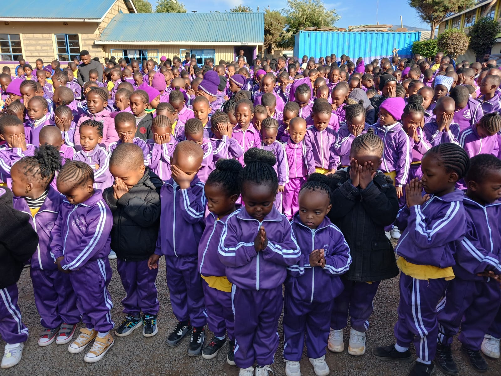 Learners in purple uniforms gathered outdoors for prayer at school